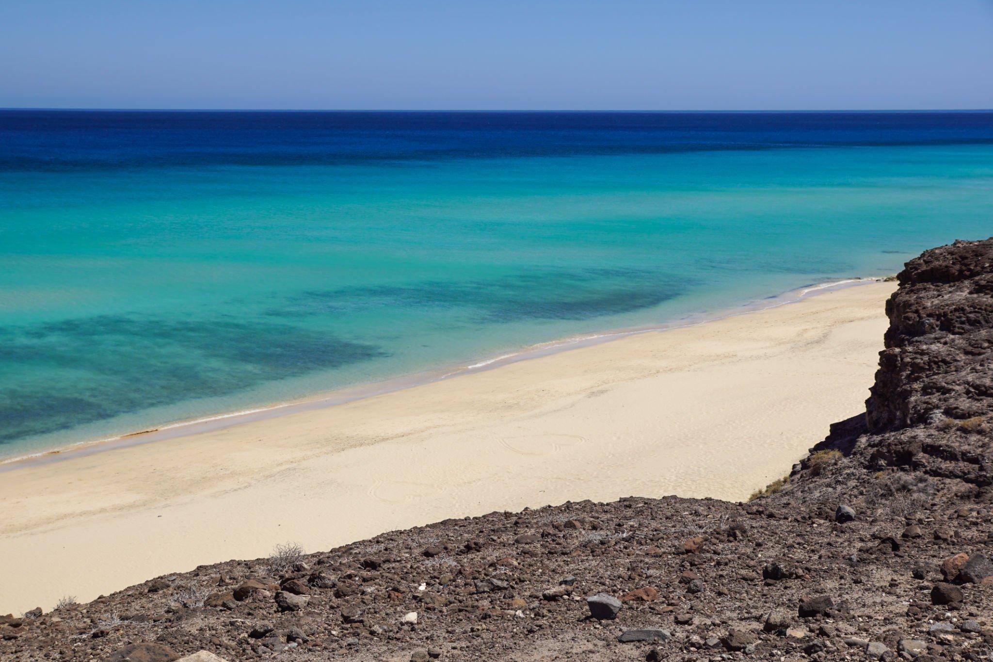 Playa de arena blanca y agua turquesa vista desde un acantilado en Jandía